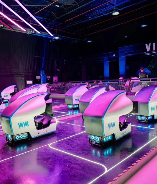 Modern racing simulator venue featuring multiple high-end racing rigs, immersive LED displays, and groups of guests enjoying competitive motorsport gameplay in a lounge-style environment.